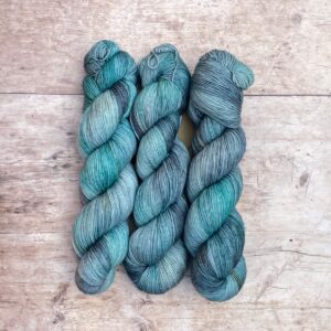 Three skeins classic sock in shades of blue, grey and turquoise on pale wood surface