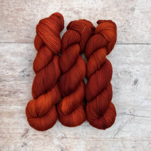 Three skeins of rusty orange Classic Sock yarn on pale wood background