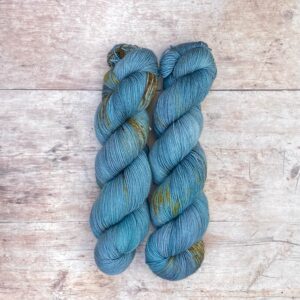 Two skeins classic sock in mid blue and teal with tan speckles on pale wood surface