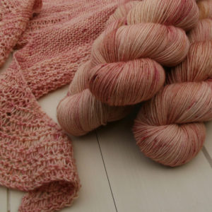 Three skeins of pink yarn and the edge of a shawl