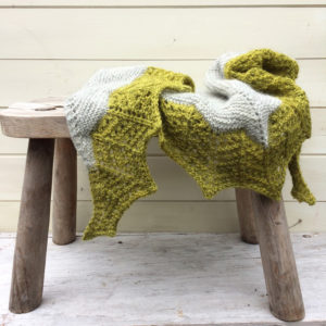 A grey shawl with an acid green lace edging draped over a stool
