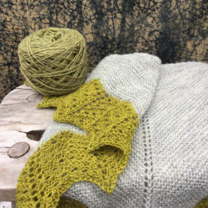 A grey shawl with acid green lace edging draped over a stool with a wound ball of paler greyer yarn