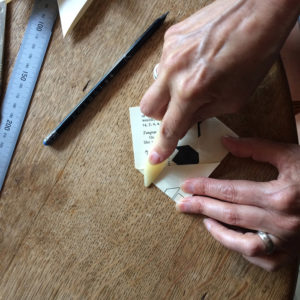 Pair of hands using a bone folder to fold an envelope on a wooden table