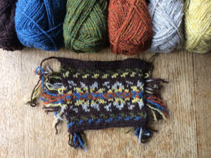 A swatch of knitted colour work with the responding coloured wool above them