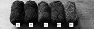 Five balls of Shetland wool lined up in a row from light to dark in black and white