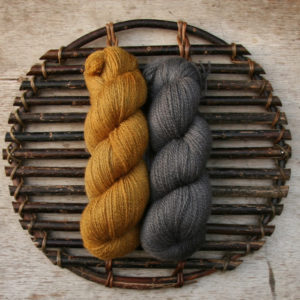 Two skeins of wool on a woven willow platter, one is a deep golden yellow and the other dark grey