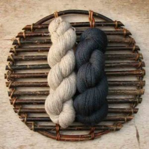 Two skeins of wool on a woven willow platter, one is dark blue the other is undyed
