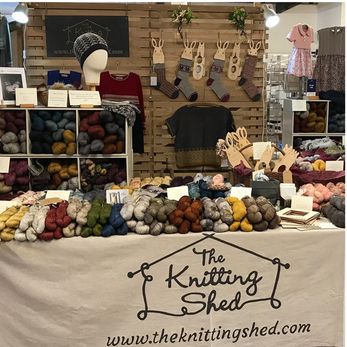 Our stand a table piled high with skeins of wool in many colours. With samples and socks hanging up behind
