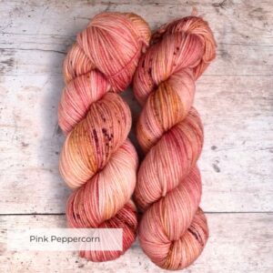 Mid mid pink variegated Plump sock yarn on a cream base with darker speckles. Sat on wood background