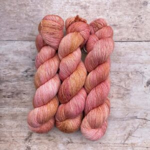 Three skeins of Merino & Silk in peach, coral and mulberry freckled with terracotta and gold