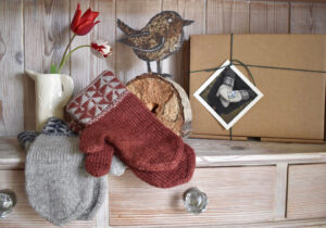 Two pairs of mittens with pattered cuffs on the shelf of a dresser