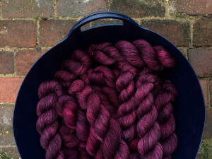 Blue bucket of rich plum coloured yarn twisted up and ready for labelling