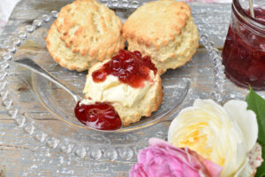 Three scones on a glass plate one split and spread with clotted cream and jam