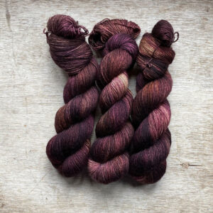 Three skeins of yarn in brown, dusty pink and bronze
