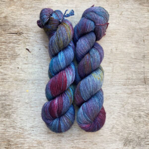 Two skeins of yarn in blues and green with splashes of dark purple and pink