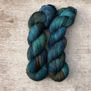 Two skeins of yarn dyed with splashes of navy, emerald and gold