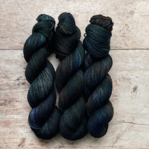 Three skeins of Plump DK in dark blue/green with splashes of brown and rust