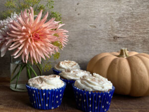 Four iced cakes next to a pumpkin and a vase of dahlias