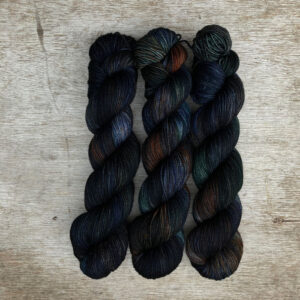 Three skeins of inky blue yarn with splashes of bottle green and rust
