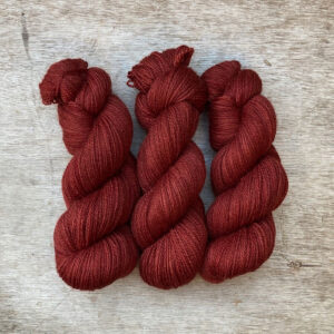 skeins of wool on a wood background. The yarn is the colour of faded red oxide