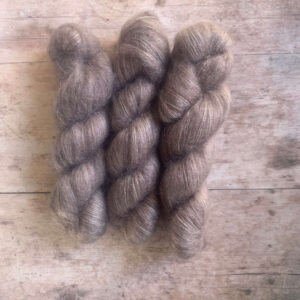 Three skeins soft light brown mohair silk yarn on pale wood background.