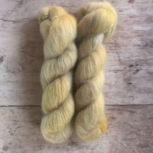 Two skeins variegated soft yellow/cream mohair silk yarn on pale wood background.