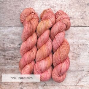 Three skeins of Plump Sock Yarn in shades of Pink on pale wood background