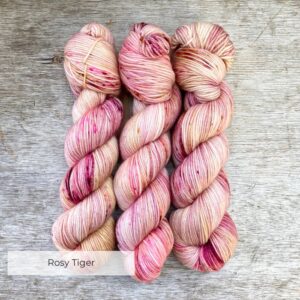 Three skeins of DK yarn in a creamy yellow speckled with dark red and pinks