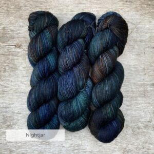 Three skeins of wool in deep greens, inky blues and rust