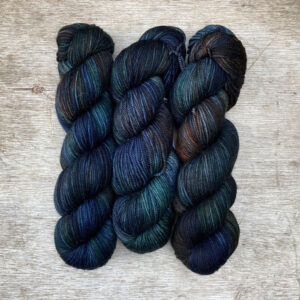 Three skeins of wool in deep greens, inky blues and rust