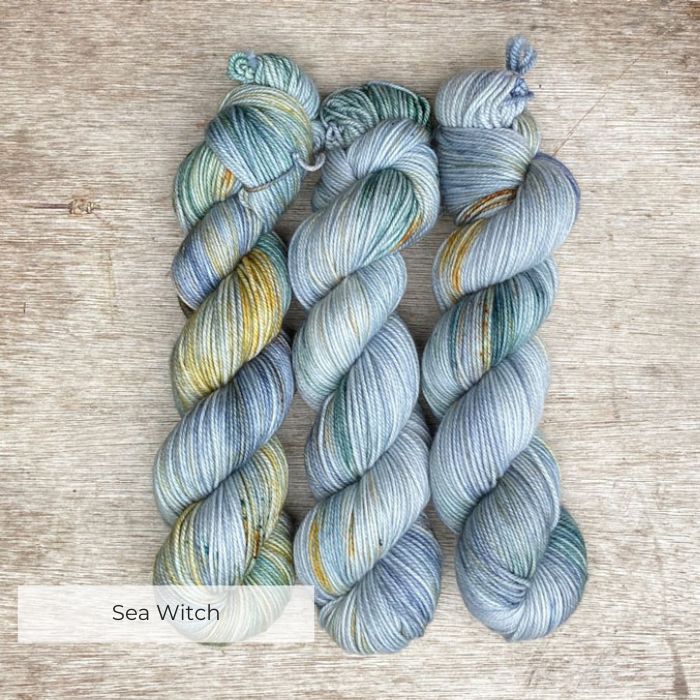 Three skeins of plump DK wool in shades of light blue and green with gold splashes