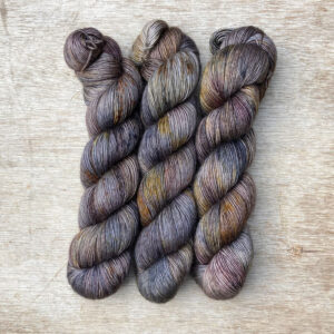 Three multicoloured skeins of wool in dark blues, plum and gold