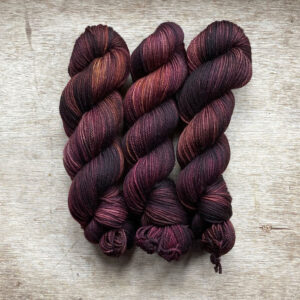 Three skeins of yarn in brown, dusty pink and bronze