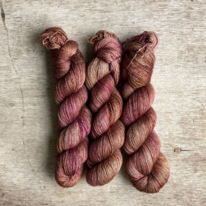 Three skeins of silky wool in shades of pink , plum and milky coffee