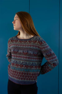 Young woman wearing Fair Isle style colour work jumper against a teal wall