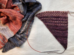 A pile of shawls with one on the needles showing the shaping