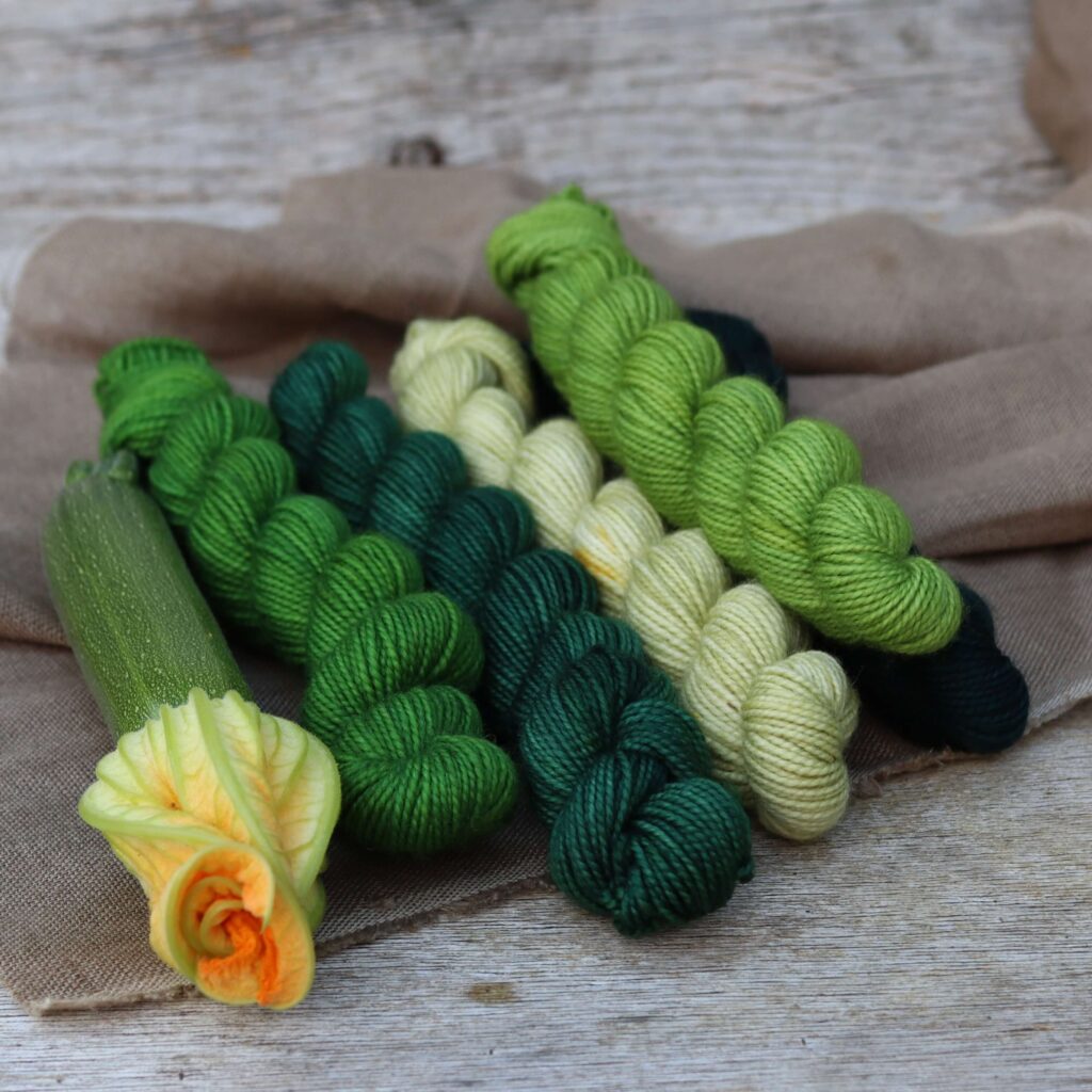 Five mini skeins of Classic sock wool in shades of green with a courgette