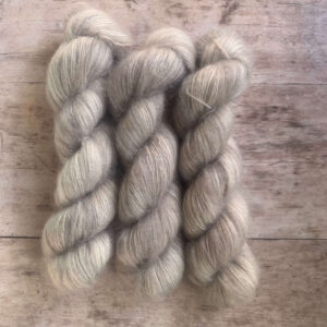 Three skeins of soft grey grey mohair and silk lace weight yarn on pale wood background