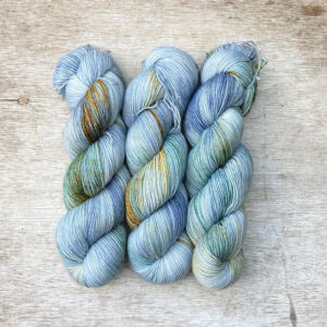 Three skeins of sock yarn in shades of blue, light grey and gold