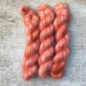 Three skeins of a deep coral yarn in a fluffy mohair