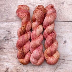 Three skeins of Merino & Silk in peach, coral and mulberry freckled with terracotta and gold