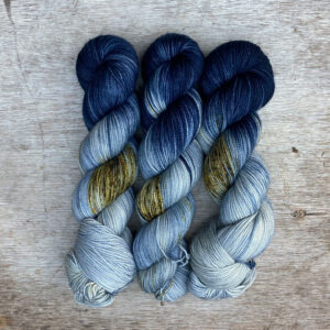 Three skeins of sock yarn in a pale speckled blue and a dark blue end