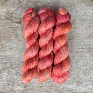 Three skeins of soft merino and mohair yarn in a deep coral and pink