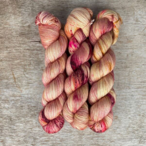Three skeins of merino mohair yarn in a creamy yellow speckled with dark red and pinks