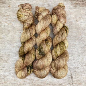 Three skeins of silky soft sand coloured yarn splashed with dark green and specks of gold