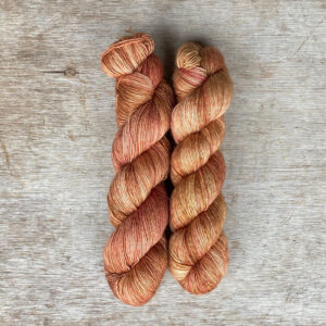 Two skeins of silky yarn in a warm yellow splashed with coral and toffee