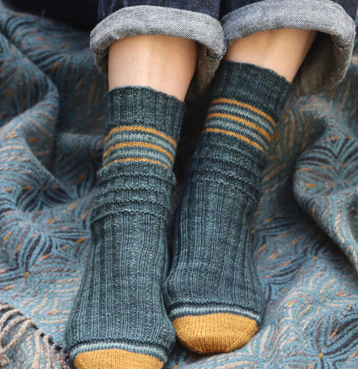 A pair of jean clad women's legs wearing striped blue socks on a blue woven blanket