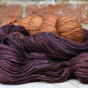 A rusty gold skein of silky merino resting on another unwound skein in purple brown
