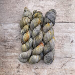 Three skeins of Feather in grey, cream, yellow and orange speckled silky yarn