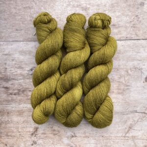 Three skeins of silk merino yarn in a yellow-green on pale wood background